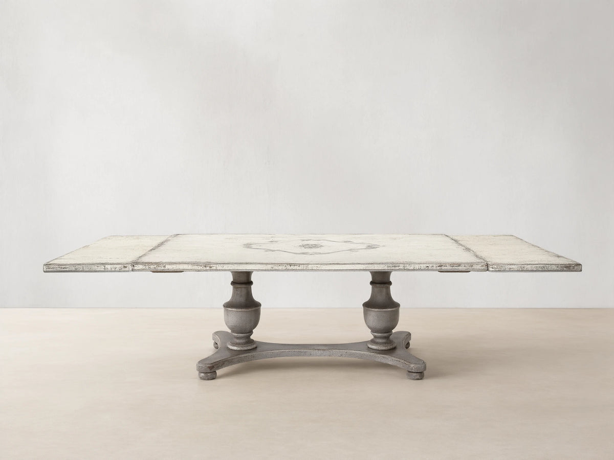 Biancca Bell'Arte rectangular dining table with distressed Antique White top, Antique Grey floral scroll, and pedestal base.