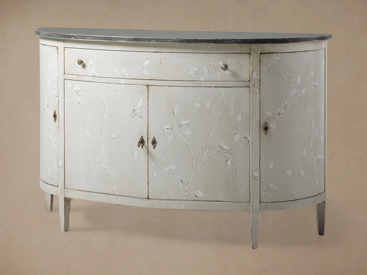 Sofia Bell'Arte Demilune Cabinet with a curved design, white finish, delicate bird motifs, and a dark top. Features one drawer and two doors.
