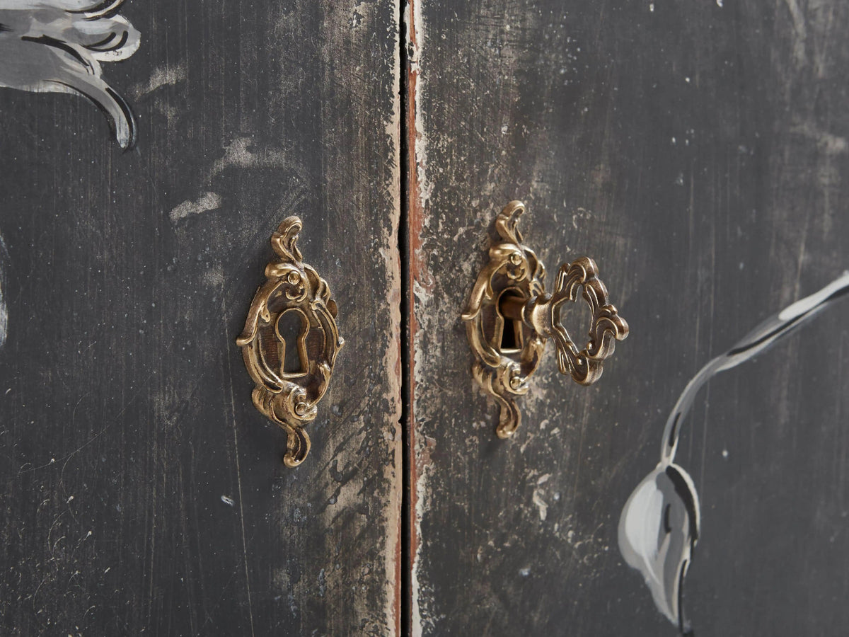 Demilune cabinet with hand-painted bird and vine motifs on a distressed dark finish, curved front, and tapered legs.