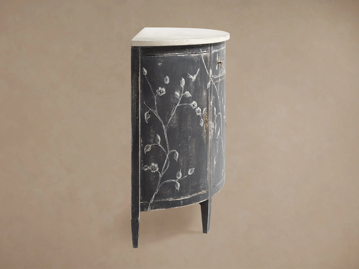 A close-up of the Sofia Bell'Arte Demilune Cabinet, showcasing a hand-painted bird motif in grayscale on a dark, distressed surface.