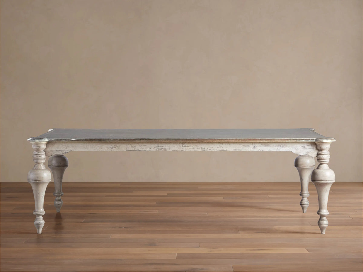 Alessia Bell'Arte Dining Table with distressed ivory, grey & beige base, ornate hand-carved legs, and a dark grey top on wood.