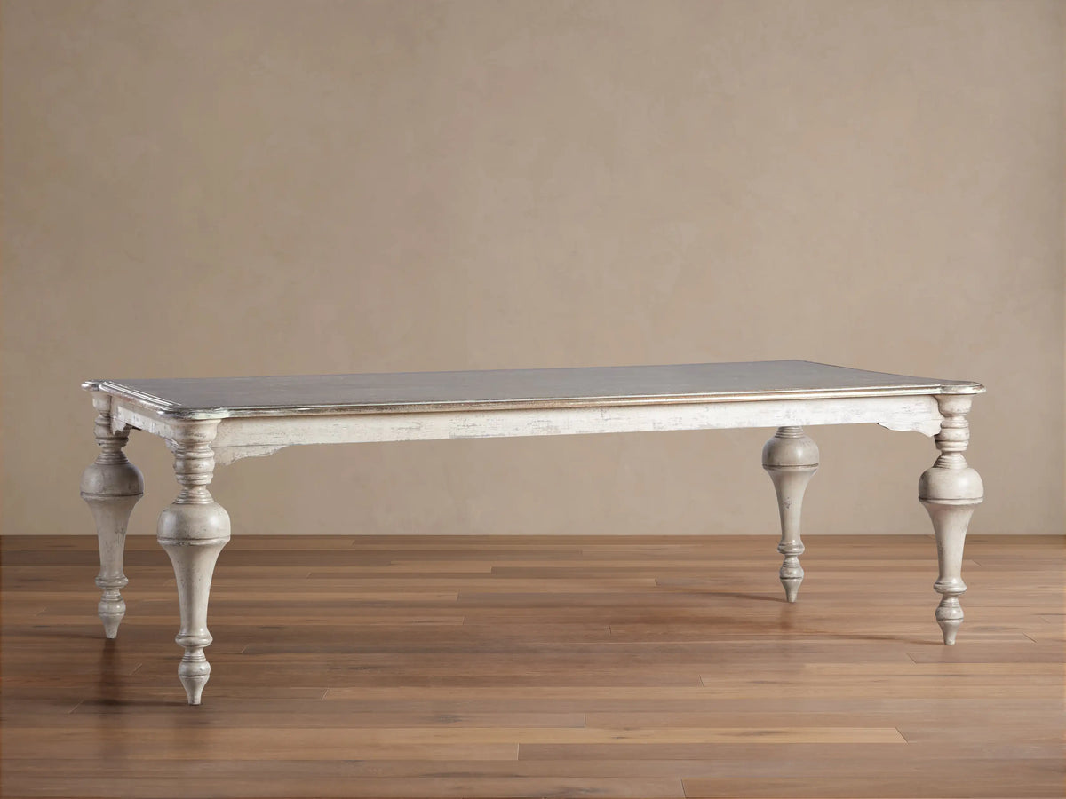 Alessia Bell‚ÄôArte Dining Table: Dark grey rectangular top, distressed antique ivory/beige carved base & legs on wood floor.