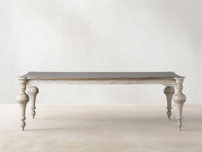 Alessia Bell'Arte Dining Table with distressed ivory, grey & beige base, ornate hand-carved legs, and a dark grey top on wood.