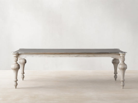 Alessia Bell'Arte Dining Table with distressed ivory, grey & beige base, ornate hand-carved legs, and a dark grey top on wood.