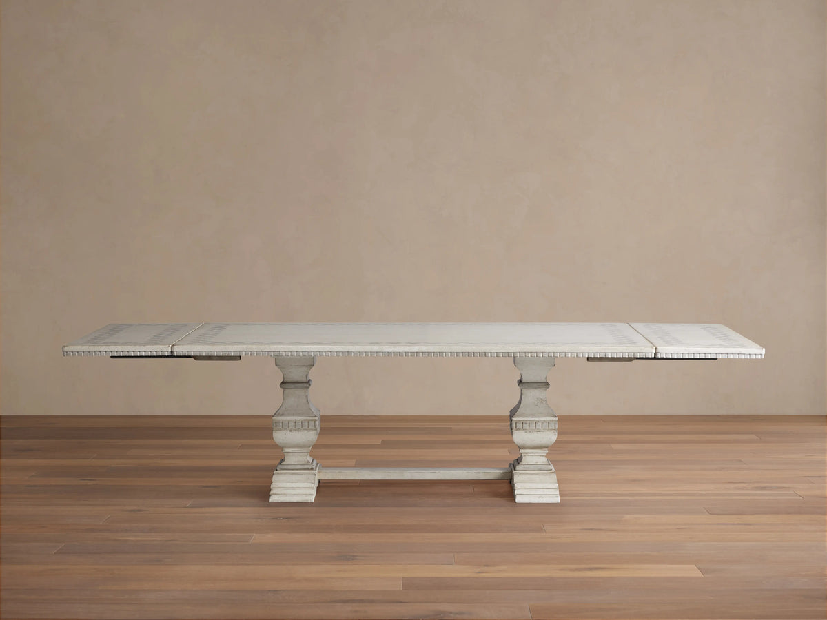 Distressed white Cerea Ribbon Bell'Arte Dining Table, hand-painted border, two pedestals, leaves partially extended.