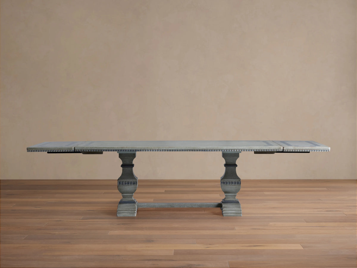 Cerea Gallery Bell'Arte Dining Table in distressed gray finish with ornate carved pedestal legs and rectangular top, on wood floor.