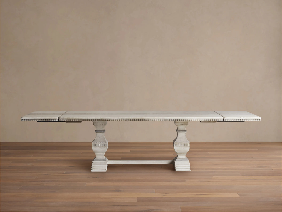 Cerea Amalfi Bell'Arte Dining Table with a distressed white finish, intricate hand-painted runner, and two extensions in a spacious wooden room.