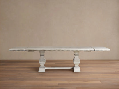 Cerea Amalfi Bell'Arte Dining Table with a distressed white finish, intricate hand-painted runner, and two extensions in a spacious wooden room.