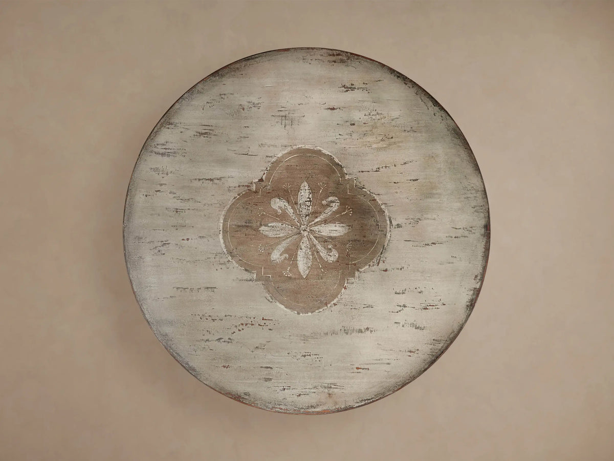 Florence Bell‚ÄôArte Round Dining Table. Distressed ivory grey top with central floral design, dark rust carved pedestal base.
