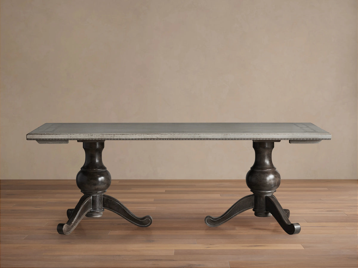 Girardi Geo Link Bell'Arte Dining Table featuring a long rectangular top in Antique White with an Antique Grey geometric border, supported by two ornate dark pedestal legs on a wooden floor.