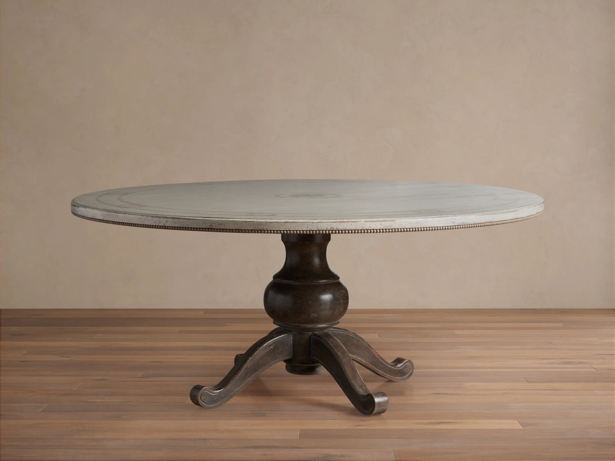 Round dining table with Antique White top, dark curved pedestal base on wooden floor, hand-painted geometric border.