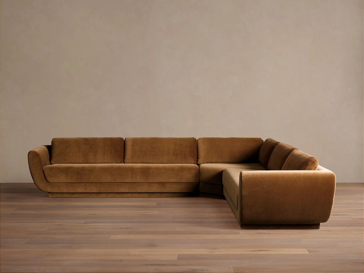 Fontana Corner Sectional, L-shaped, upholstered in warm brown velvet with curved arms, shown on a wooden floor.