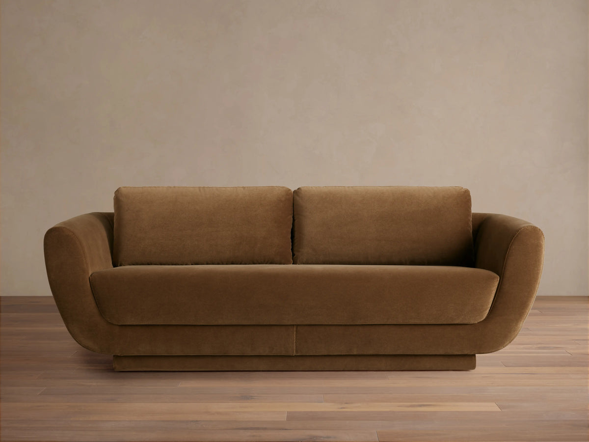 Front view of the brown Fontana Sofa, a two-seater with rounded arms, loose back cushions, and a low, solid base.