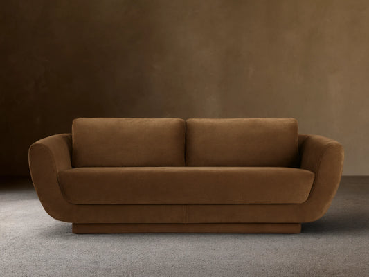 Front view of the brown Fontana Sofa, a two-seater with rounded arms, loose back cushions, and a low, solid base.
