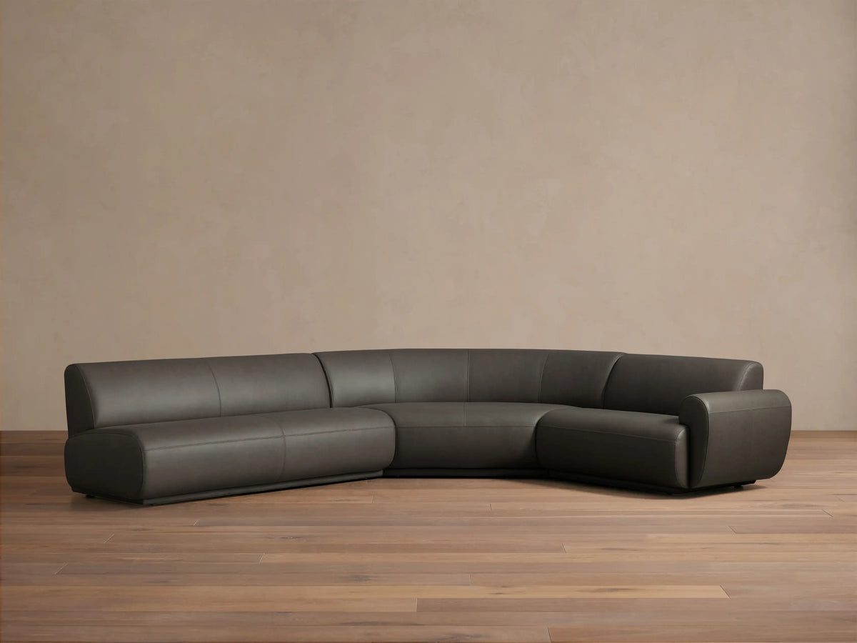 Front view of the Charcoal Gianni Leather Three-Piece Sectional, an L-shaped sofa featuring a curved right section.