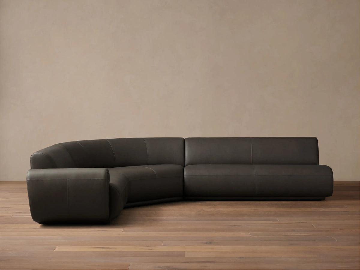 Front view of the dark gray Gianni Leather Three-Piece Sectional with a curved left arm and straight right sections.