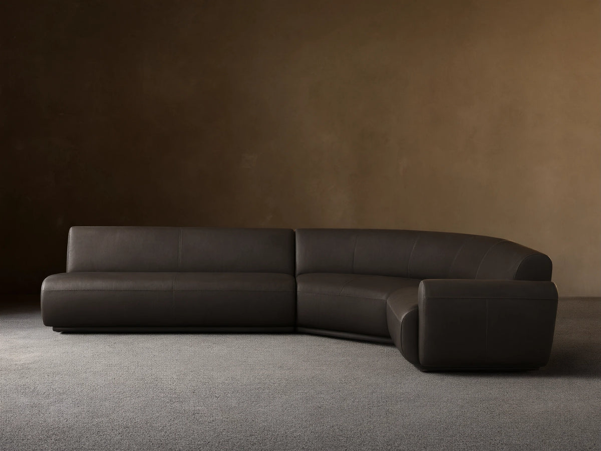 Front view of the dark gray Gianni Leather Three-Piece Sectional with a curved left arm and straight right sections.