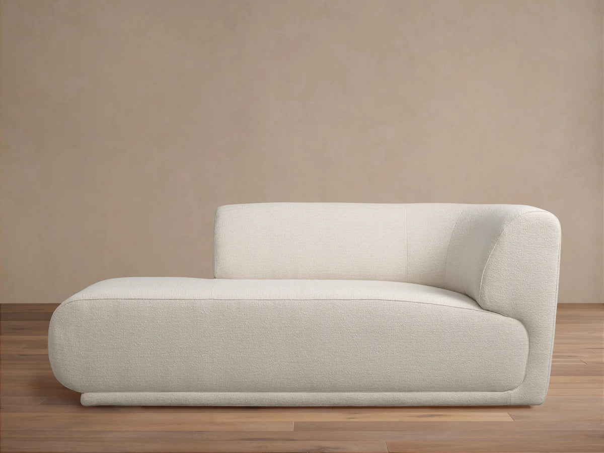 Light cream Gianni Chaise with a low, rounded design and textured fabric, backrest on the right, on a wood floor.