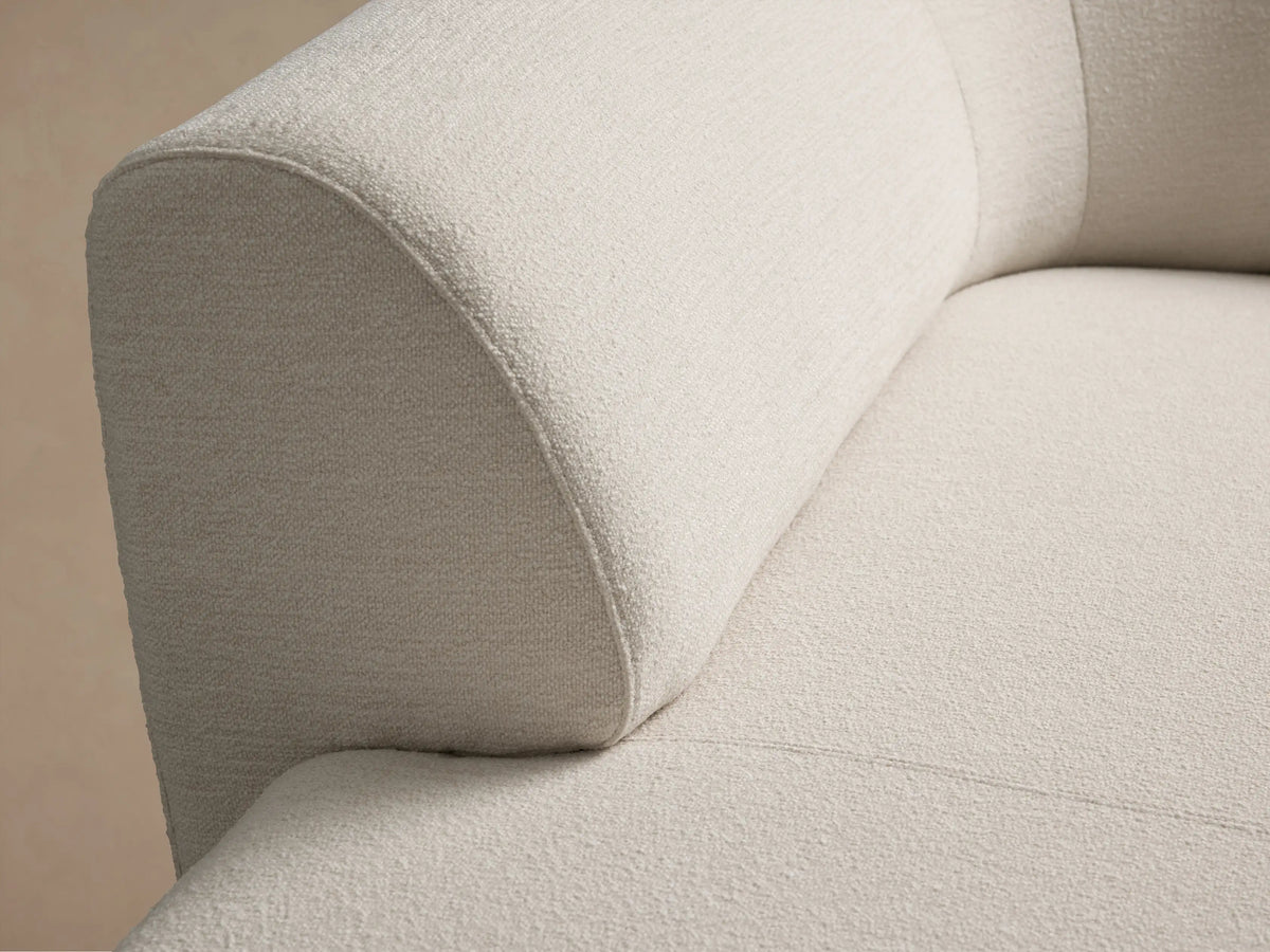 Close-up of the Gianni Chaise's light beige textured fabric, showing a rounded backrest connecting to the seat.