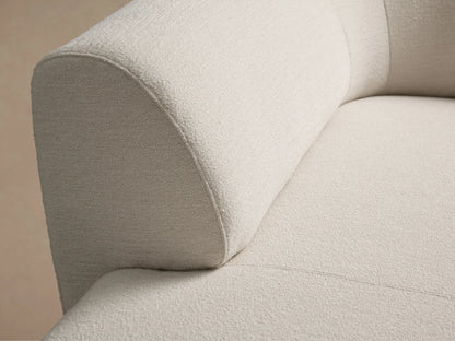 Close-up of the Gianni Chaise's light beige textured fabric, showing a rounded backrest connecting to the seat.