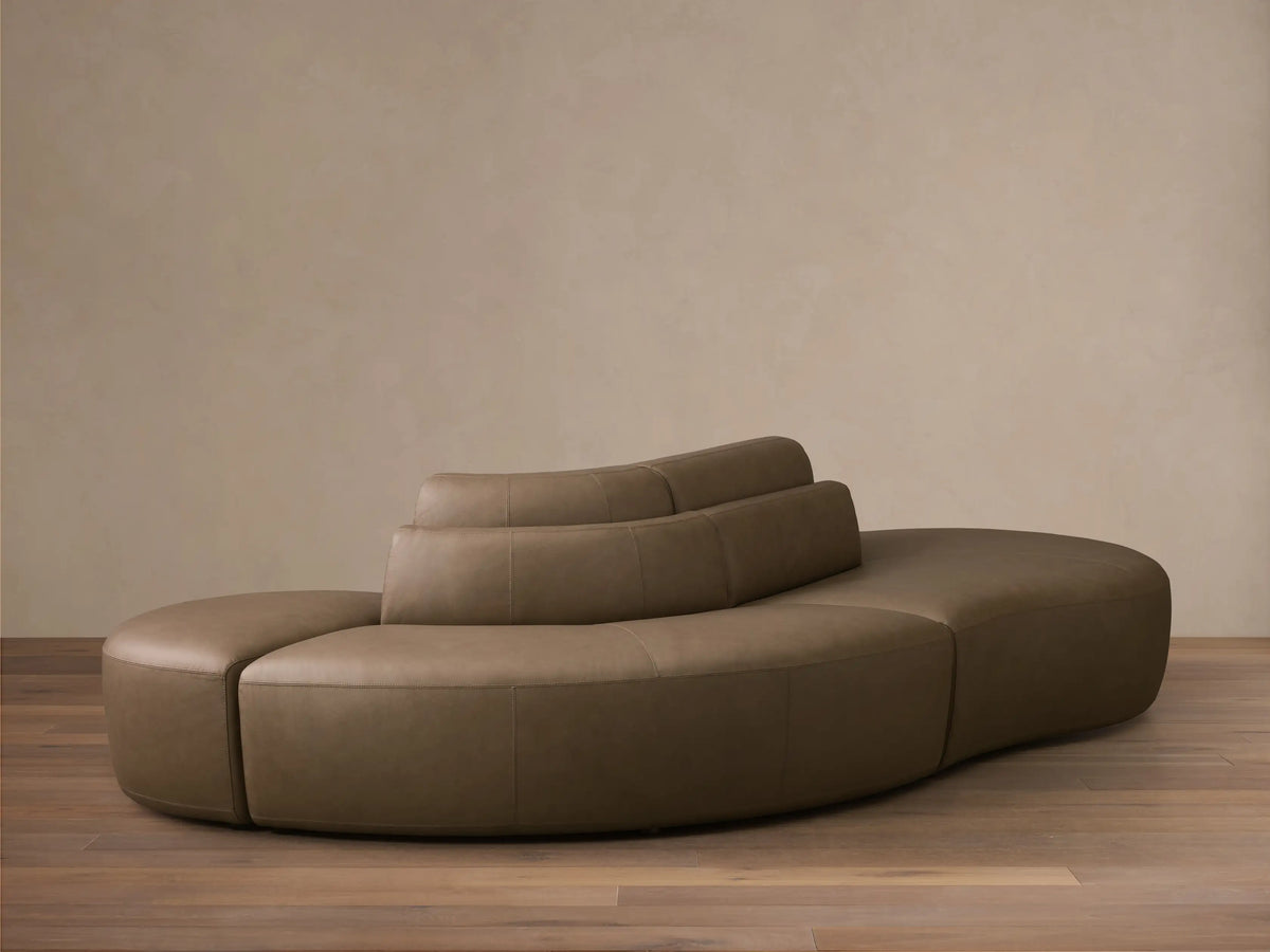 Front view of the taupe Lovina Leather Three-Piece Sectional with Ottoman, showing its curved modular design.