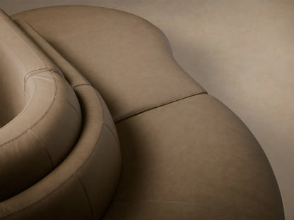 Front view of the taupe Lovina Leather Three-Piece Sectional with Ottoman, showcasing its curved, modular design.