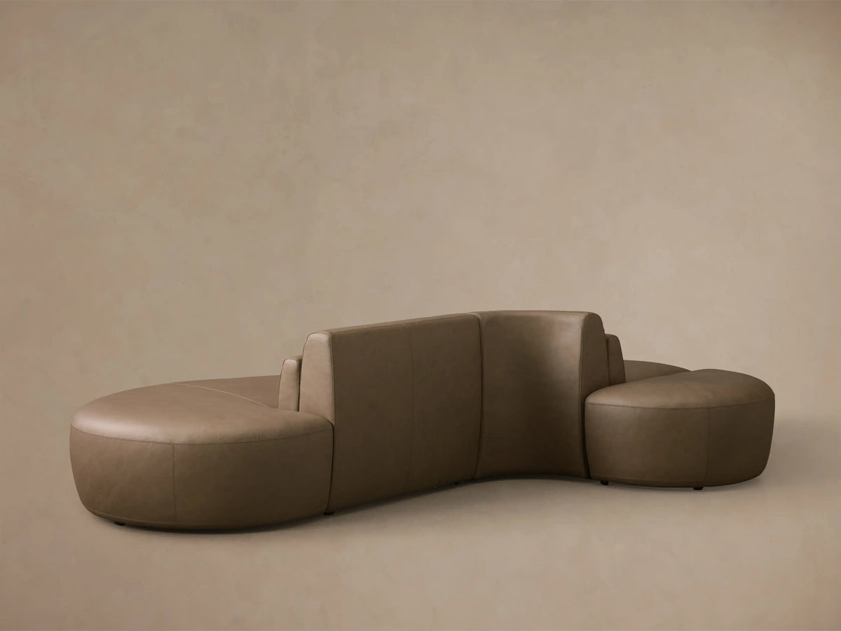 Close-up of the light brown leather on the Lovina Leather Three-Piece Sectional with Ottoman, showing a curved armrest with visible stitching.