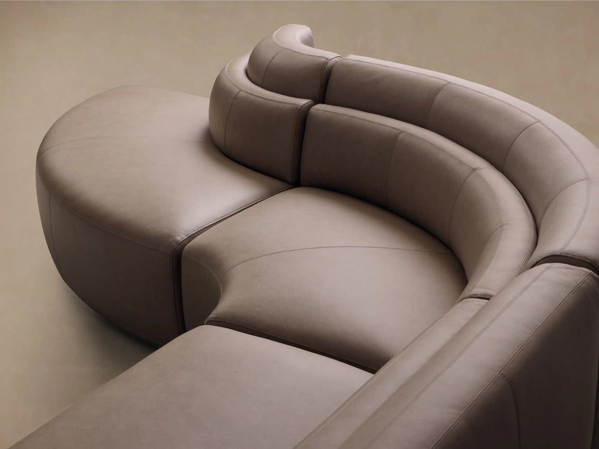 Angled view of a taupe Lovina Leather Four-Piece Bumper Sectional's curved, modular design.