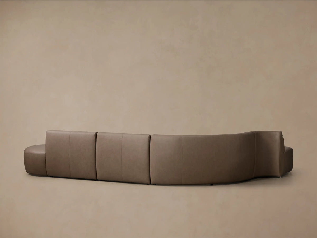 Front view of the taupe Lovina Leather Four-Piece Bumper Sectional, showcasing its elegant curved design and distinct sections.
