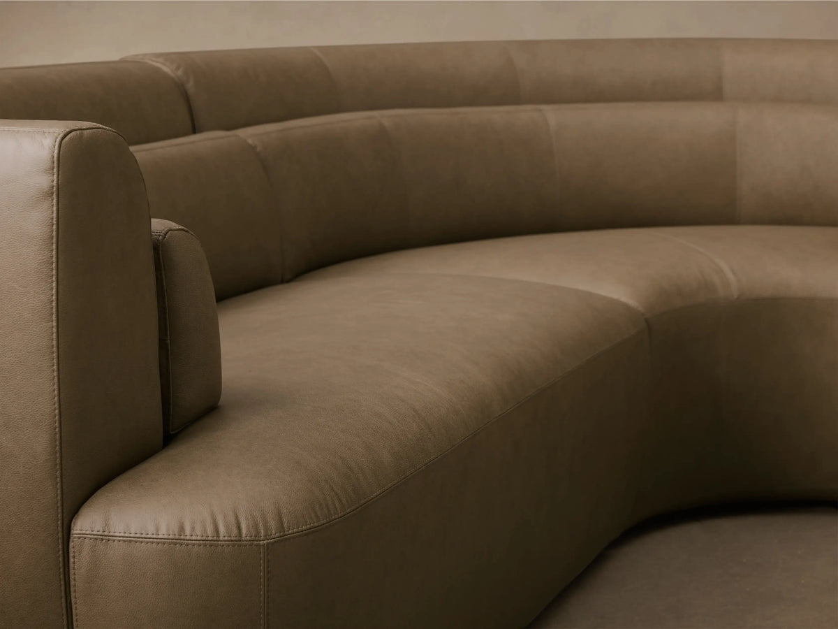 Front view of the curved olive green Lovina Leather Four-Piece Sectional with Ottoman, showing its soft leather and rounded shape.