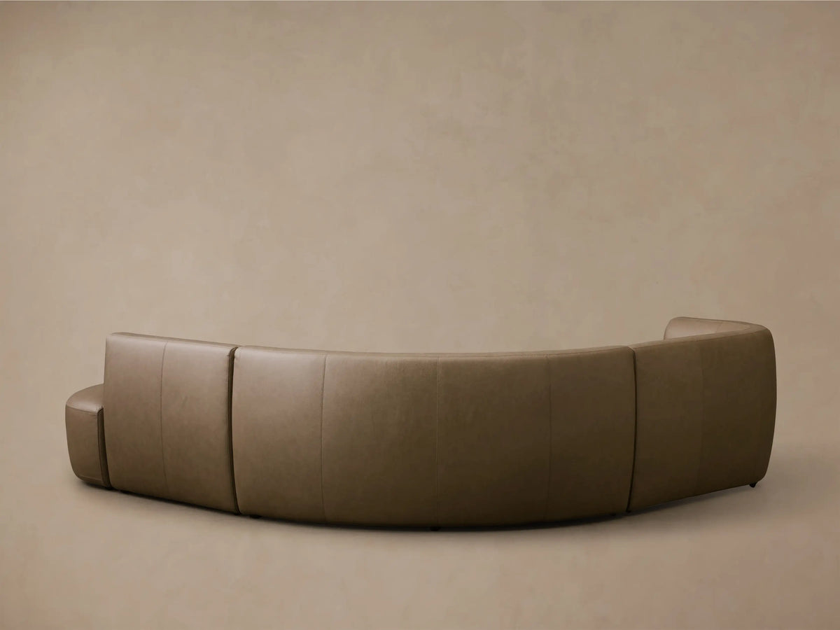 Close-up of a curved section of the Lovina Leather Four-Piece Sectional with Ottoman in taupe leather.