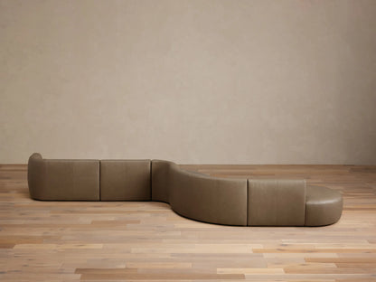 Front view of the taupe Lovina Leather Five-Piece Sectional, a modular, curved sofa with five sections on a light wood floor.