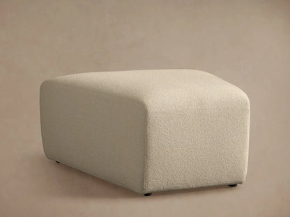 Lovina Ottoman close-up: light beige, finely textured fabric on a rounded upholstered corner, against a soft background.