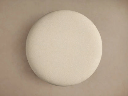 Close-up of Lovina Ottoman showing light beige, textured upholstery fabric with a subtle seam on its plush, curved surface.