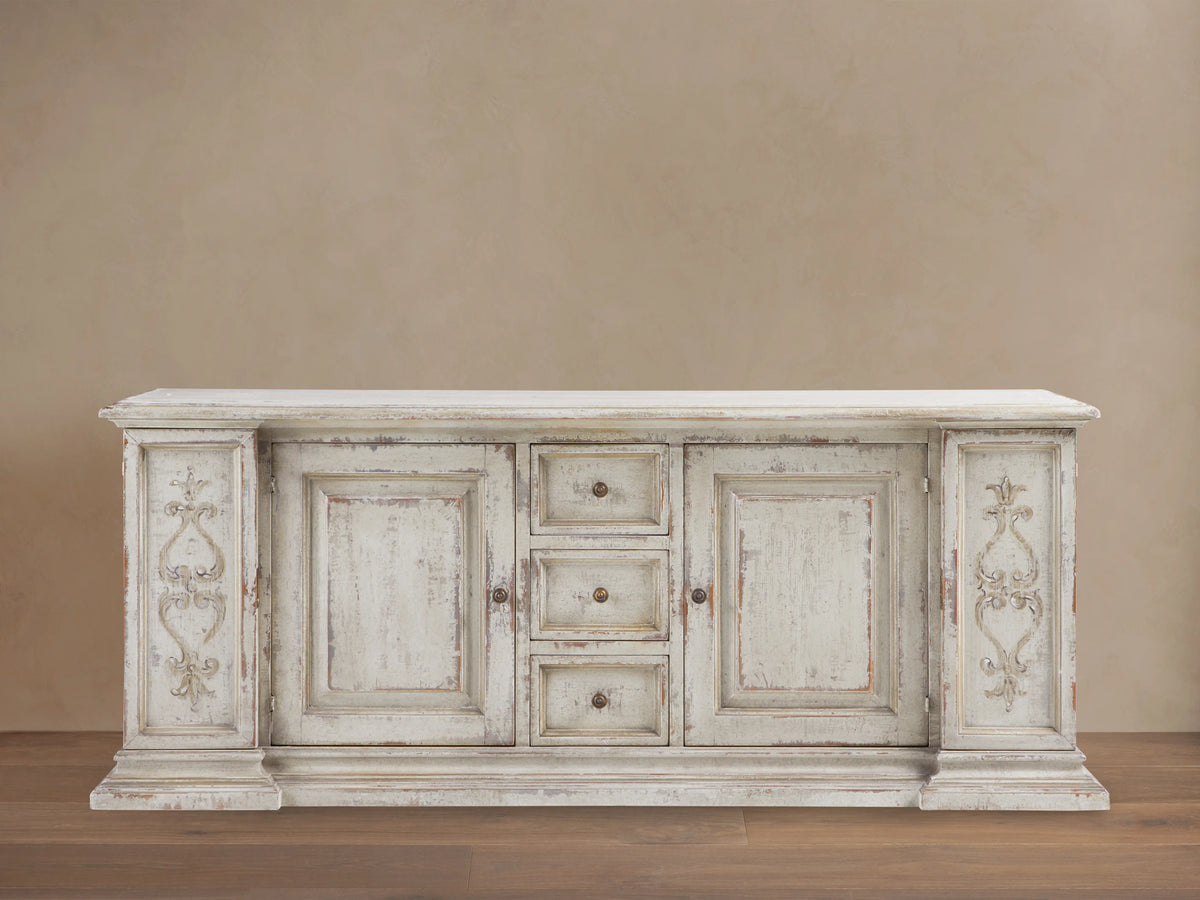 Vittoria Bell'Arte Console with hand-carved ivory grey and dark rust finish, ornate door detailing, brass knobs, and wood grain texture.