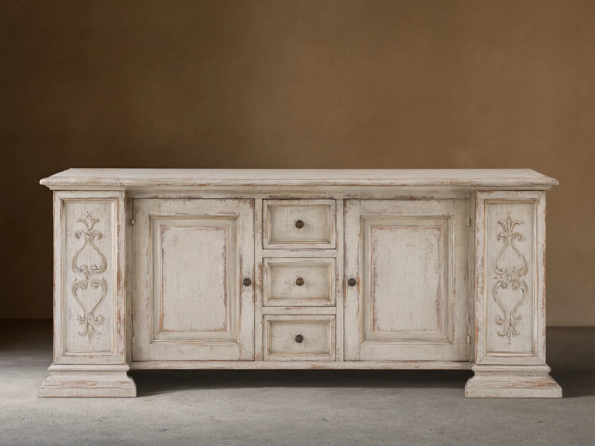 Vittoria Bell'Arte Console with hand-carved ivory grey and dark rust finish, ornate door detailing, brass knobs, and wood grain texture.