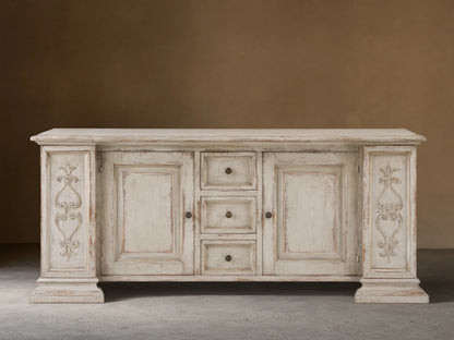 Vittoria Bell'Arte Console with hand-carved ivory grey and dark rust finish, ornate door detailing, brass knobs, and wood grain texture.