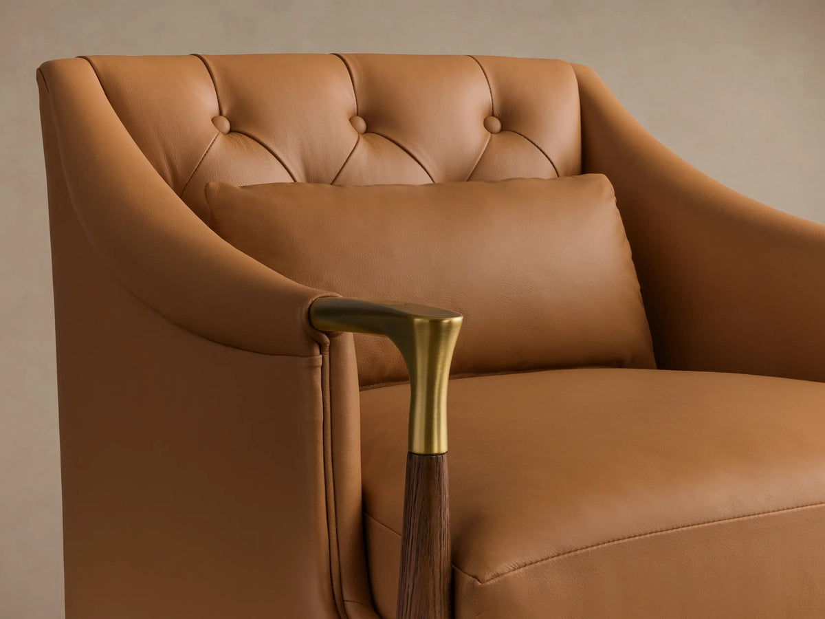 Front view of the tan leather Fisher Leather Club Chair with a tufted back, lumbar pillow, dark wood legs, and gold accents.