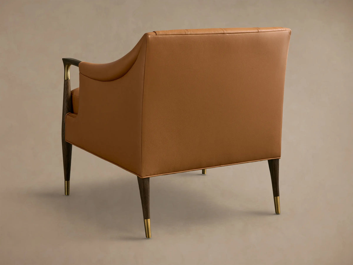 Close-up of a Cognac Fisher Leather Club Chair, showing its tufted back, matching lumbar pillow, and brass and wood armrest.