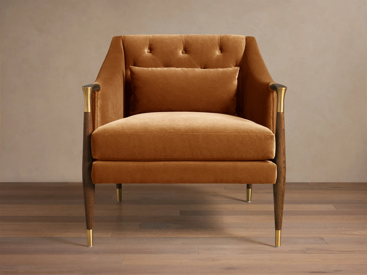 Front 3/4 view of a golden velvet Fisher Club Chair with a tufted back, matching lumbar pillow, dark wood legs, and brass accents.