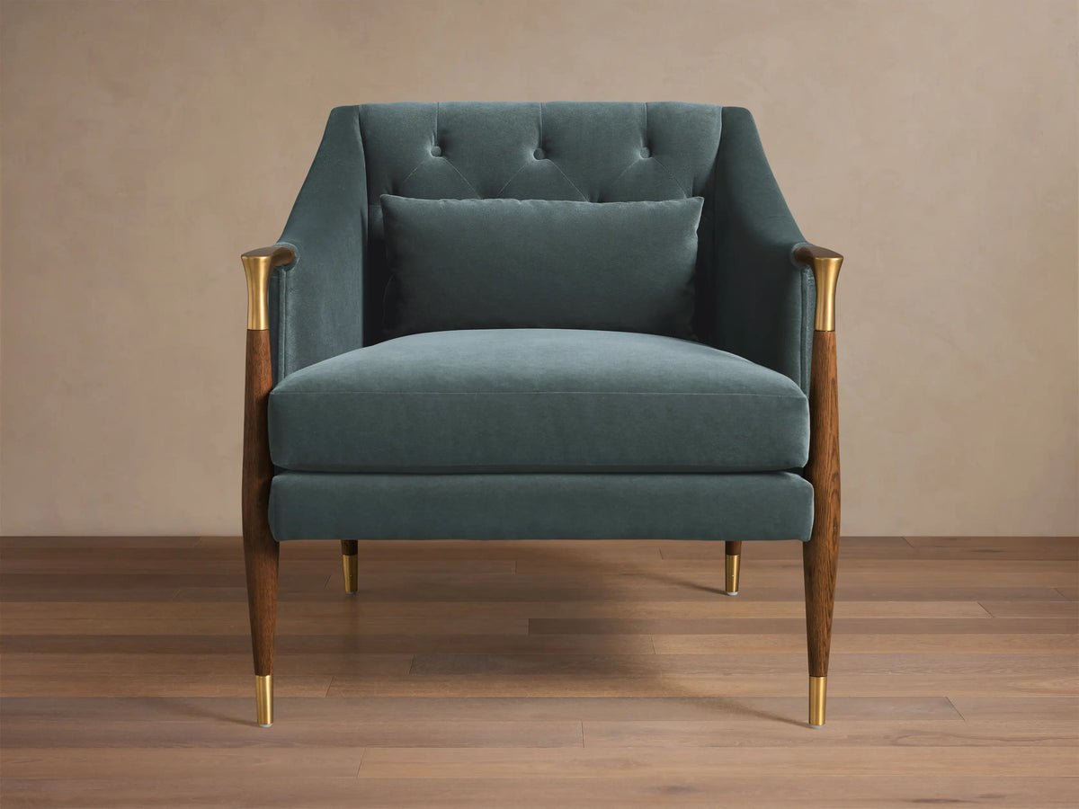 Front view of the teal velvet Fisher Club Chair with tufted back, coordinating lumbar pillow, wooden arms with brass accents, and wooden legs with brass caps.