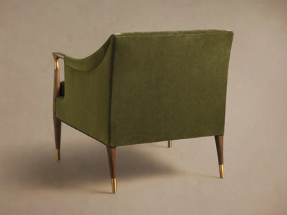 Angled front view of an olive green Fisher Club Chair with velvet upholstery, tufted back, wooden arms with brass accents, and a lumbar pillow.