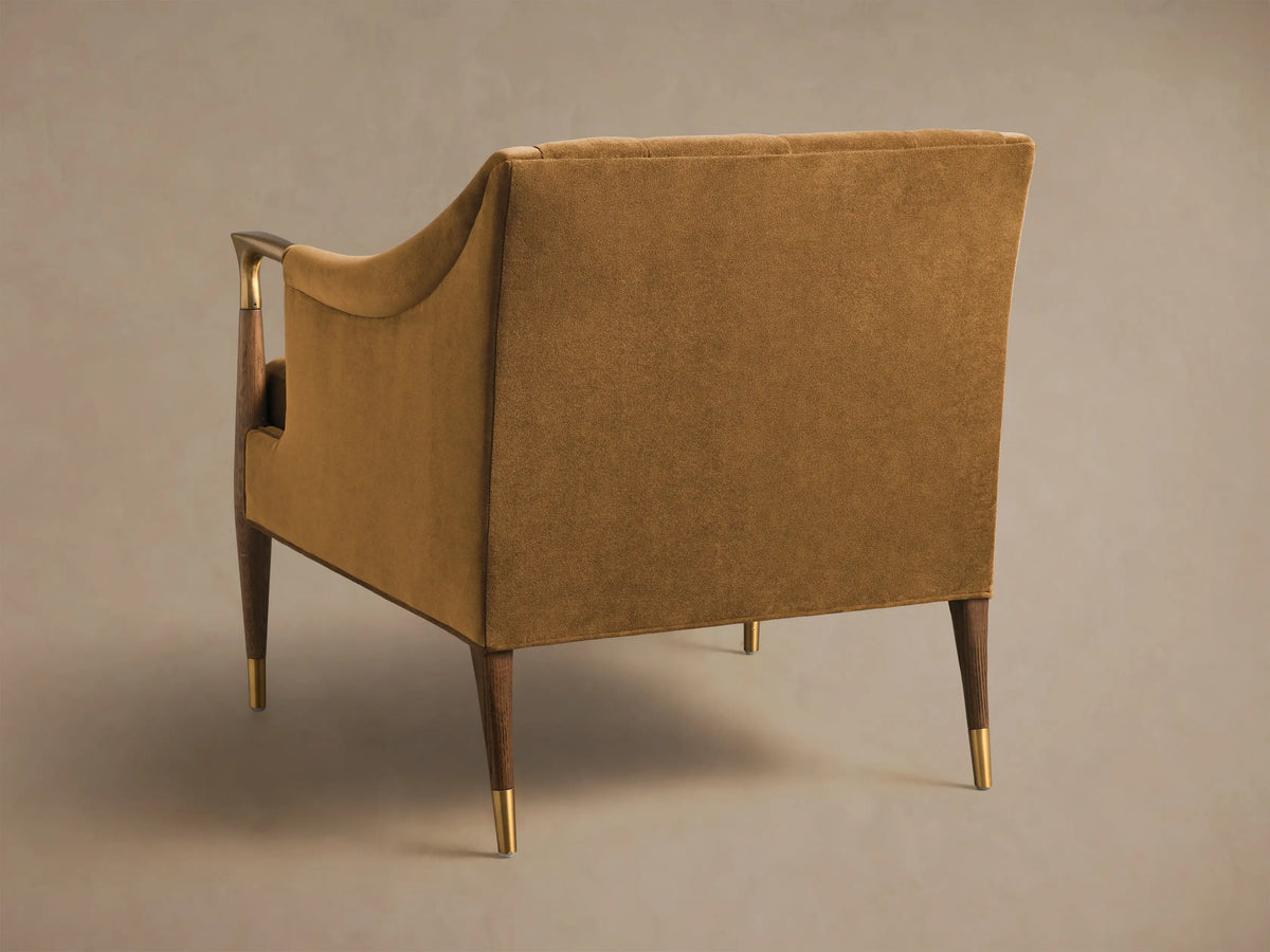 Rear 3/4 view of a golden-brown Fisher Club Chair with dark wooden legs featuring brass caps and a matching wooden armrest with brass accent.