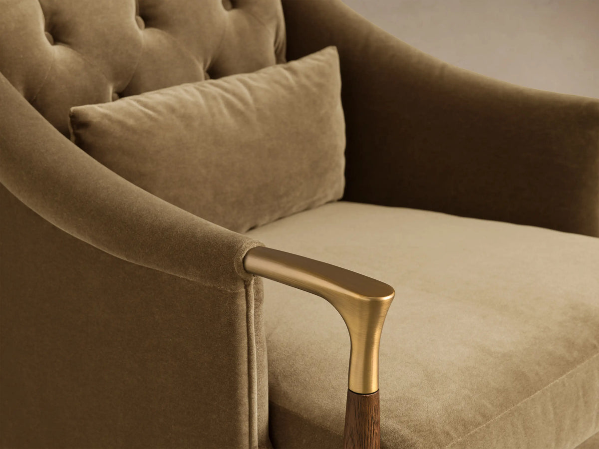 Close-up of the golden brown velvet Fisher Club Chair, showing its tufted back, lumbar pillow, and brass and wood armrest.