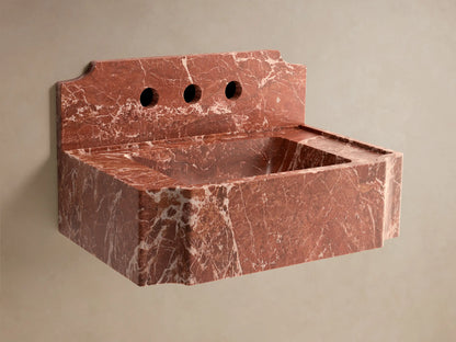 Front view of a red honed stone Dottie Wall-Mounted Sink with Backsplash with white marbling and chrome faucet.