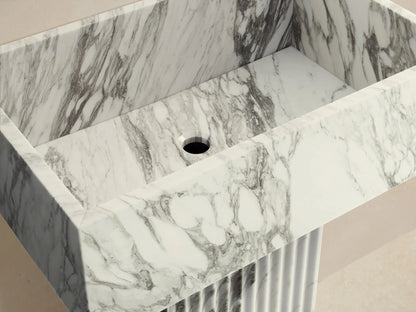 Front view of the white and grey marble Riven Pedestal Sink, featuring a rectangular basin and fluted base. A faucet is above it.