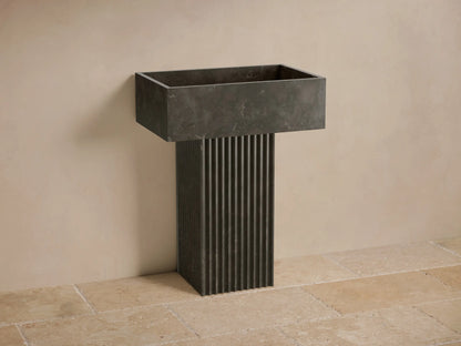 Front view of a dark gray natural stone Riven Pedestal Sink with a fluted base and integrated rectangular basin.