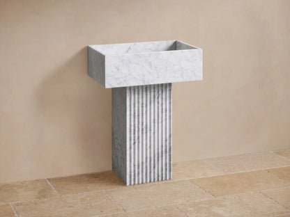 Front view of a rectangular white marble wall-mounted sink with a vertically fluted pedestal.