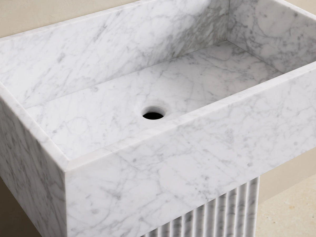 Front view of a white marble fluted pedestal sink featuring a rectangular basin and a base with vertical ribbed detailing.