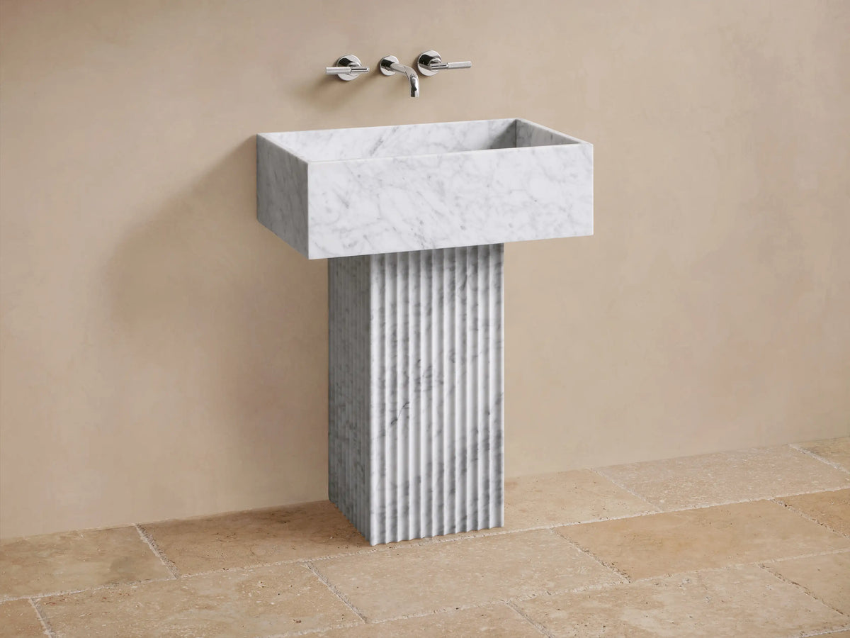 Close-up of white marble rectangular sink with grey veining and a black drain hole, featuring a fluted marble base.